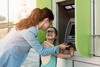 a woman showing her young daughter how to use an automated banking machine